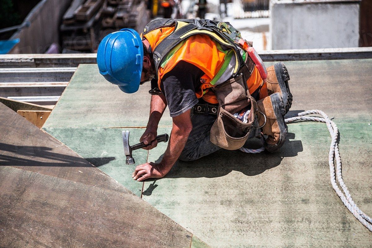 Roofer in a harness nailing down roof decking